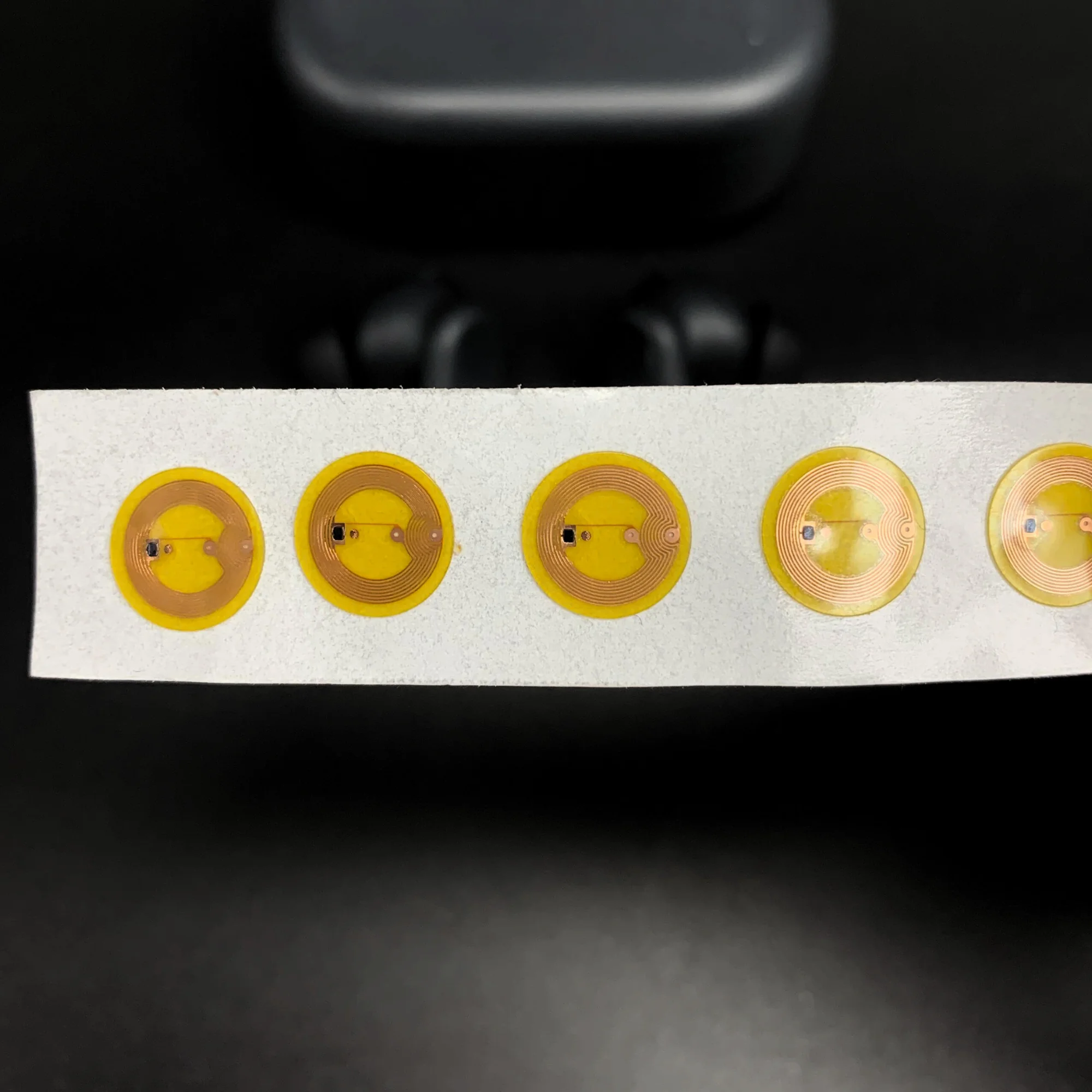 A strip of five circular yellow NFC stickers with visible copper coils on a dark background.