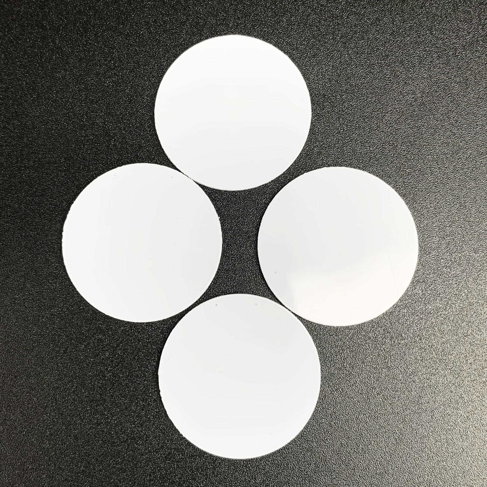 White circular NFC coin tags with a smooth surface, placed on a black textured background.